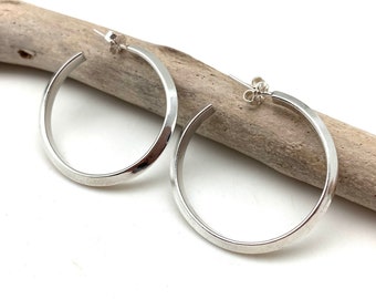 Könnte beinhalten: Ein Paar silberne Creolen mit gehämmerter Oberfläche. Die Ohrringe sind schlicht und elegant und eignen sich hervorragend als Geschenk für jeden Anlass.