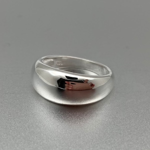 May include: A silver ring with a smooth, rounded surface. The ring is wide and has a polished finish.