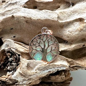 May include: A rose gold pendant featuring a tree of life design with an iridescent opal inlay.