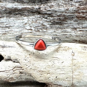 May include: A silver ring with a triangular red coral stone. The ring is marked with the number "S76".