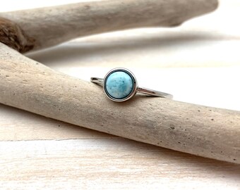 May include: A silver ring with a light blue gemstone set in a bezel setting.