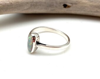 Könnte beinhalten: Ein silberner Ring mit einem weißen Opal-Edelstein. Der Ring ist schlicht und elegant.