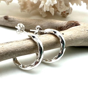 May include: A pair of silver hoop earrings with a hammered texture. The earrings are small and delicate, and they would be a great addition to any jewelry collection.