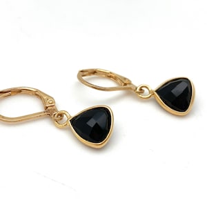 May include: A pair of gold-colored leverback earrings, each featuring a triangular, black gemstone. The gemstones are set in a gold-colored bezel. The earrings are displayed against a white background.