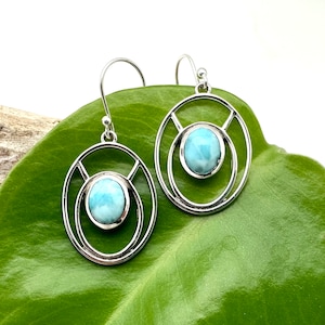 K&ouml;nnte beinhalten: Ein Paar silberne Ohrringe mit einem blauen Edelstein in der Mitte jedes Ohrrings. Die Ohrringe haben ein kreisf&ouml;rmiges Design mit einem kleineren Kreis innerhalb des gr&ouml;&szlig;eren Kreises.