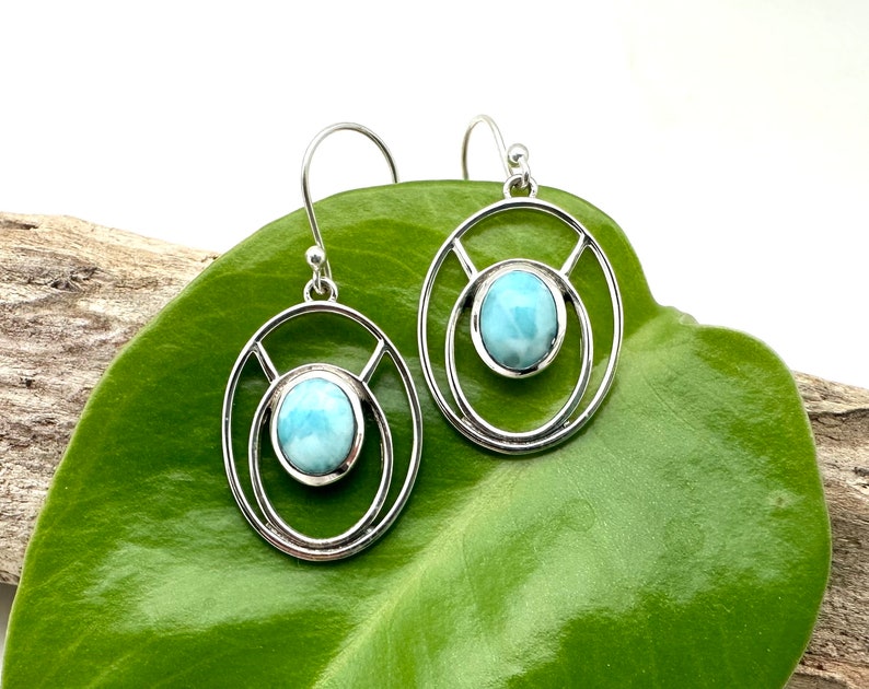 K&ouml;nnte beinhalten: Ein Paar silberne Ohrringe mit einem blauen Edelstein in der Mitte jedes Ohrrings. Die Ohrringe haben ein kreisf&ouml;rmiges Design mit einem kleineren Kreis innerhalb des gr&ouml;&szlig;eren Kreises.
