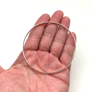 May include: A silver bangle bracelet, shown in a person's hand.