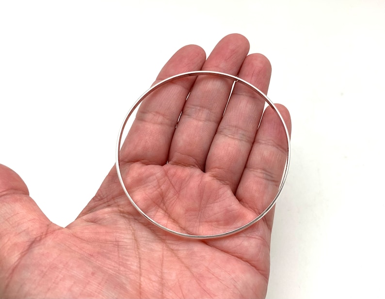 May include: A silver bangle bracelet, shown in a person's hand.