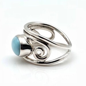 May include: A silver ring with a light blue, oval-shaped stone. The ring features a unique design with swirling, openwork details. The stone is set in a bezel setting, and the band has a split shank design.
