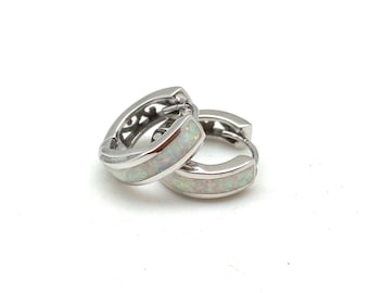 May include: A pair of silver-colored hoop earrings with a white opal-like inlay. The earrings have a hinged closure and a decorative cutout design on the top. The earrings are displayed on a white background.