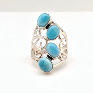 May include: A silver ring with a delicate, swirling design set with four oval-shaped blue gemstones.