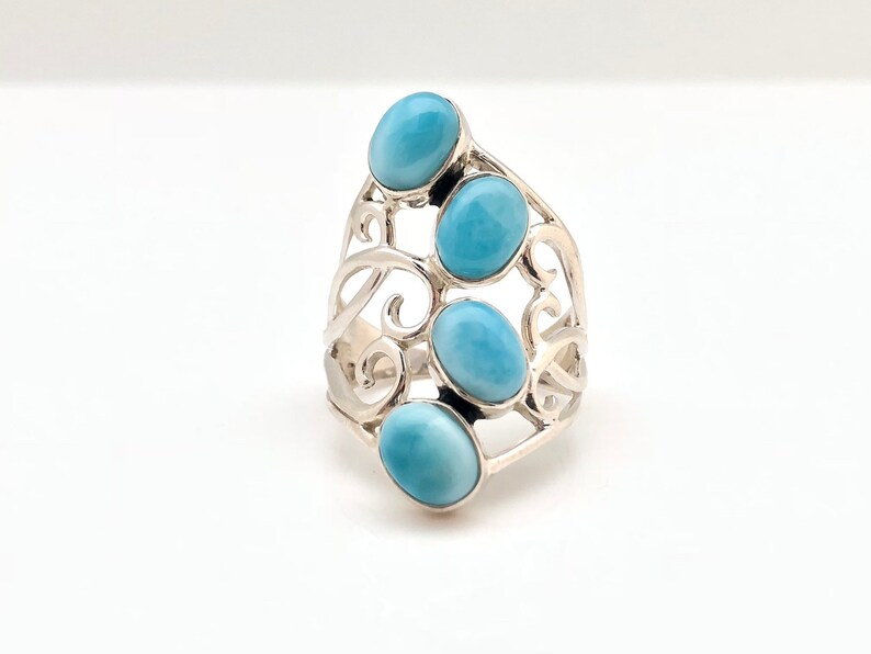 May include: A silver ring with a delicate, swirling design set with four oval-shaped blue gemstones.