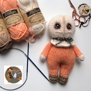 May include: A knitted doll with a white face, orange body, and brown shoes. The doll has large black eyes and a black bow tie. The doll is surrounded by yarn balls and knitting needles.