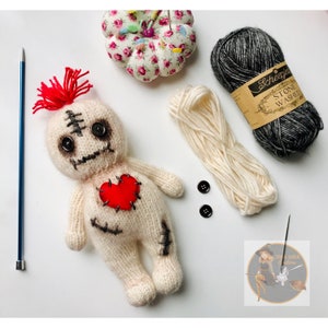 Op de afbeelding: Een witte gebreide voodoopop met rood garen haar, zwarte knoopjesogen en een rood vilt hart. De pop is omringd door garen, knopen en een naald. De afbeelding bevat ook een klein logo met de tekst "Stone Witch Creations".