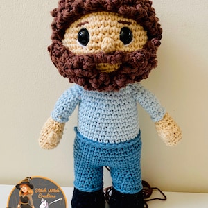 May include: Crocheted amigurumi doll with brown hair, a beard, a blue shirt, blue jeans, and black shoes.