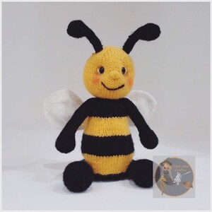 May include: A knitted bee toy with black and yellow stripes, white wings, and a smiling face. The bee is sitting on a white surface.