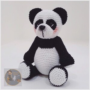 May include: A crocheted panda bear plush toy with black and white fur. The panda has black eyes, a black nose, and pink cheeks.