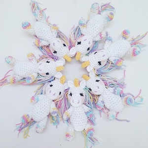 May include: Seven crocheted unicorn toys with rainbow yarn manes and tails. The unicorns are white with black eyes and yellow horns.