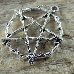 May include: Silver pendant in the shape of a pentagram, made of twisted branches. The pendant is on a wooden surface.