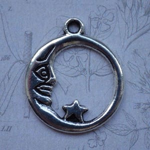 Puede incluir: Encanto de plata en forma de media luna con una estrella en su interior. La luna tiene una cara tallada.