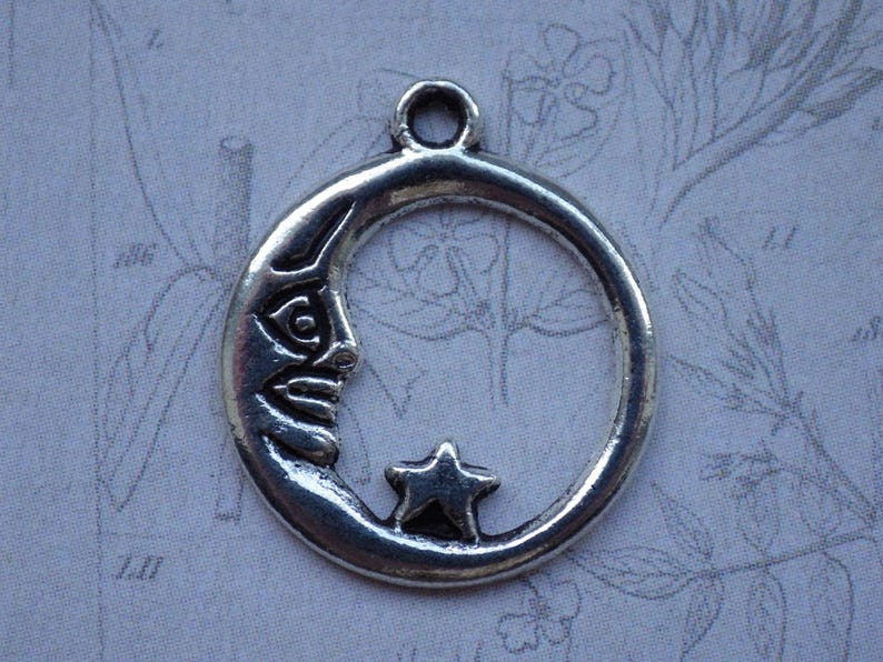 Puede incluir: Encanto de plata en forma de media luna con una estrella en su interior. La luna tiene una cara tallada.