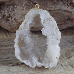 May include: White geode pendant with a gold-toned bail. The geode has a large opening that reveals the crystal formations inside.