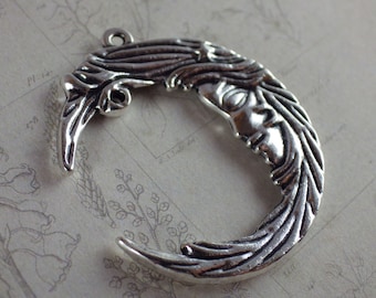 May include: A silver-coloured crescent moon pendant featuring a woman's face. The moon has flowing hair and a loop for hanging. The pendant is likely metal and has an antique or vintage aesthetic. Ideal for jewellery making.