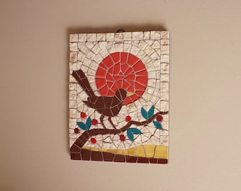 May include: A mosaic wall art featuring a brown bird perched on a branch with red berries. The bird is facing the left and has a yellow beak. The background is a white mosaic with a red circle in the center.