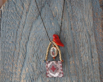 May include: A gold chain necklace with a red bird charm, a small gold frame with a religious image, and a red and white fabric pouch.