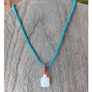 Puede incluir: Un collar de cuentas turquesa con un colgante blanco y detalles rojos.