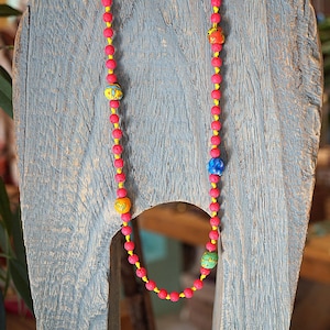 Könnte beinhalten: Eine rosa und gelbe Perlenkette mit bunten, gemusterten Perlen. Die Kette ist auf einer Holzoberfläche abgelegt.