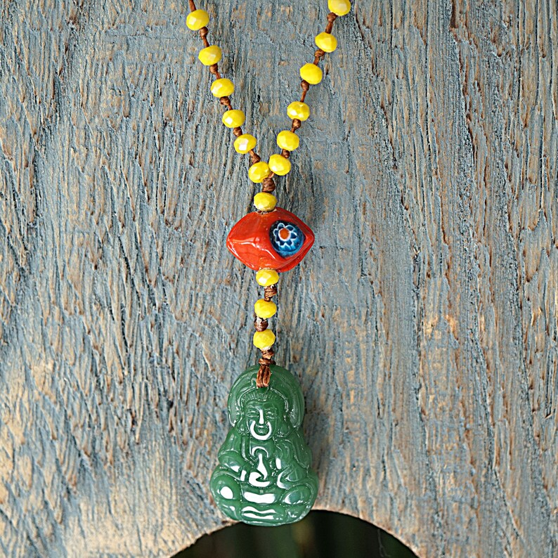 May include: A green jade Buddha pendant necklace with a red and blue eye bead and yellow beads.