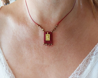May include: A red cord necklace with a small gold pendant featuring a religious image. The pendant is surrounded by small gold stars and red beads.