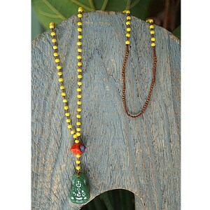 May include: A yellow beaded necklace with a green jade Buddha pendant and a red and blue bead accent. The necklace is displayed on a wooden surface.