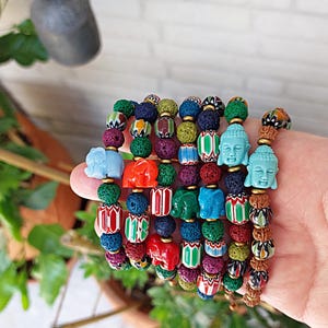 Pu&ograve; includere: Un mucchio di braccialetti colorati con perline di roccia vulcanica, perline con motivi e piccoli ciondoli a forma di elefante e Buddha.