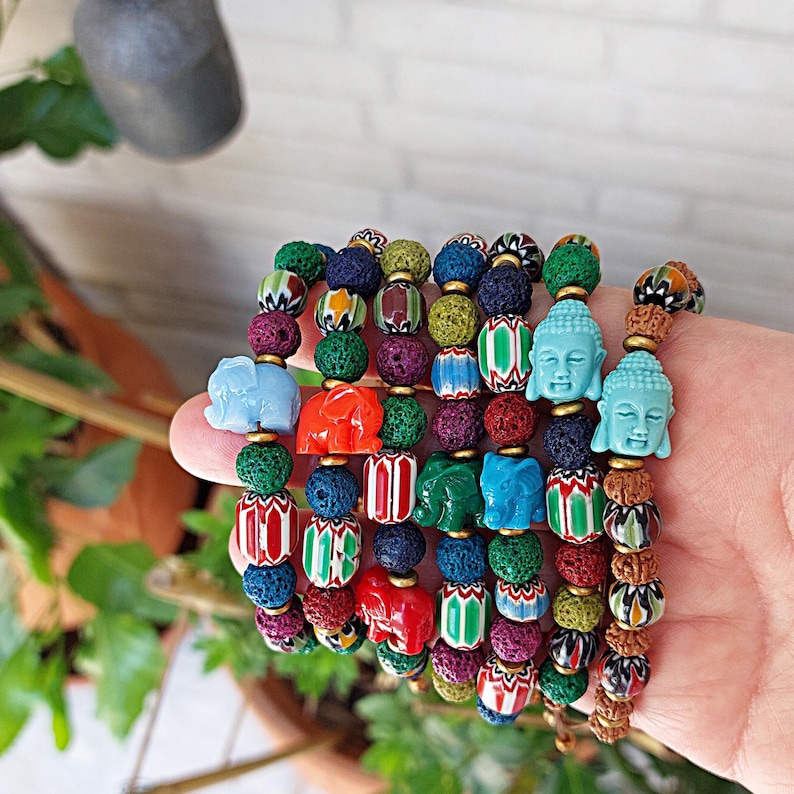 Pu&ograve; includere: Un mucchio di braccialetti colorati con perline di roccia vulcanica, perline con motivi e piccoli ciondoli a forma di elefante e Buddha.