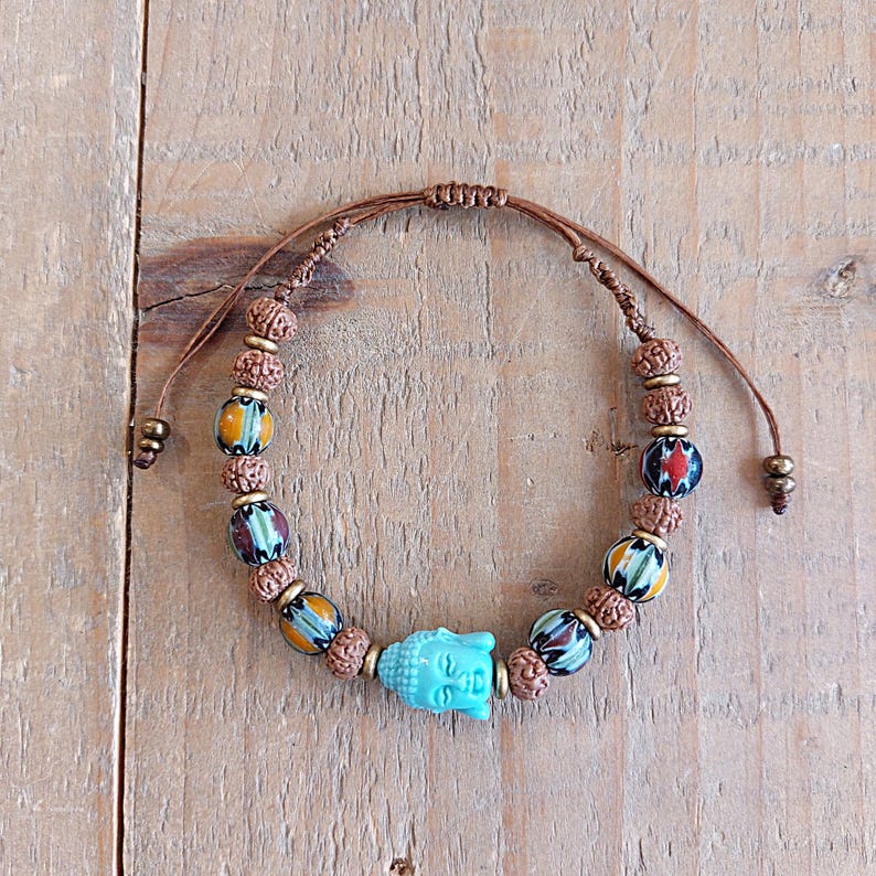 Pu&ograve; includere: Un braccialetto con un ciondolo a forma di testa di Buddha blu turchese, perline di legno marrone e perline con motivi colorati. Il braccialetto &egrave; regolabile con un nodo scorrevole.