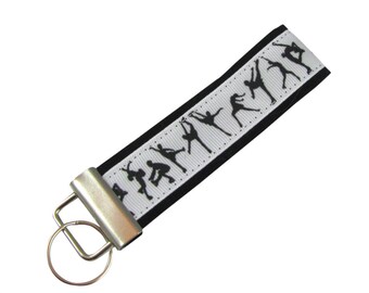 May include: A white and black key chain with a silver key ring. The key chain has a black ribbon with a white stripe and a pattern of black figure skaters on the white stripe.