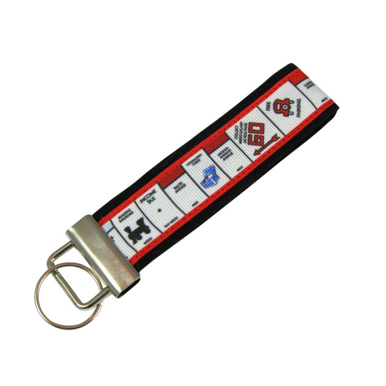 May include: A red and black key chain with a white Monopoly board design. The key chain features the iconic "GO" square and other game elements.