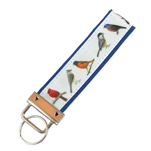 May include: A white and blue key chain with a silver key ring. The white ribbon has a pattern of colorful birds.