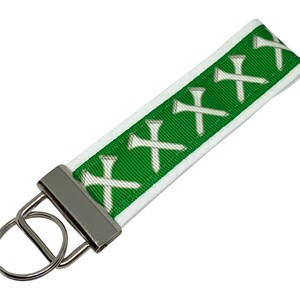 May include: White and green key chain with a silver key ring. The green ribbon has a pattern of white golf tees.