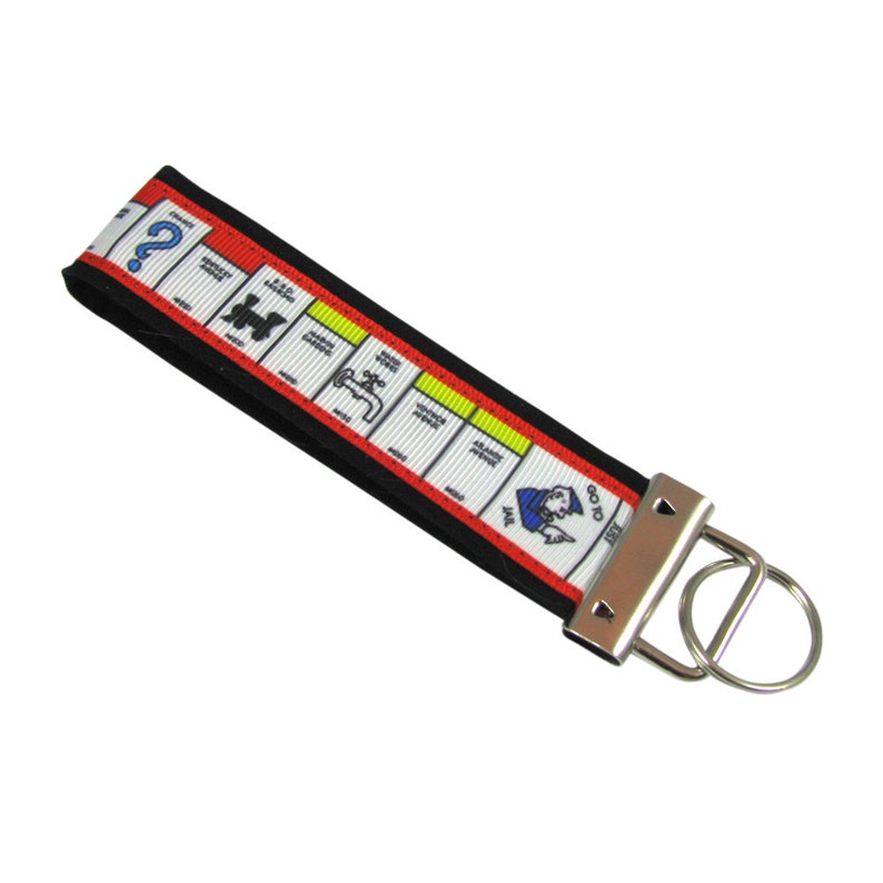 May include: A black and red keychain with a Monopoly board design. The keychain features a silver key ring and a silver clasp. The Monopoly board design includes the iconic "Go to Jail" space and other game pieces.