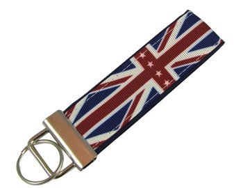 Puede incluir: Un llavero azul, rojo y blanco con un diseño de Union Jack. El llavero tiene un anillo de metal plateado y un clip de metal plateado.