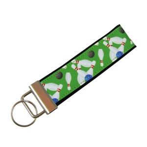 May include: Green and black key chain with a bowling pin and ball pattern. The key chain has a silver metal ring and clasp.