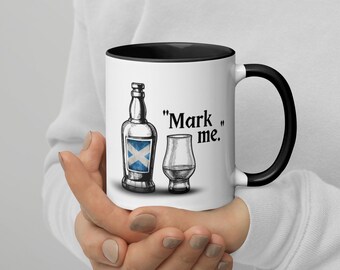 May include: White ceramic mug with a black rim and handle. The mug features a black and white illustration of a bottle of scotch with the Scottish flag on the label and a small glass of scotch. The text "Mark me." is printed on the mug.