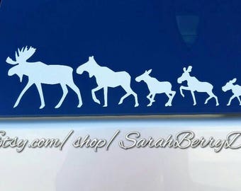 May include: White silhouette vinyl decal of a moose family with five moose in a line, walking to the right. The decal is on a blue car window. The text "www.Etsy.com/shop/SarahBerryDesigns" is at the bottom of the image.