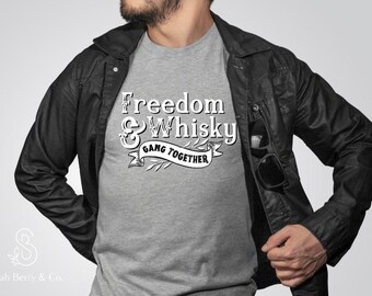 May include: A gray t-shirt with the words "Freedom & Whisky Gang Together" in white script. The shirt is worn under a black leather jacket. Sunglasses are tucked into the jacket pocket.