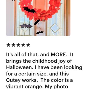 Op de afbeelding: Een rode en zwarte Halloween-krans met vleermuizen die eraan hangen. De krans is gemaakt van papier en heeft een levendige oranje kleur.