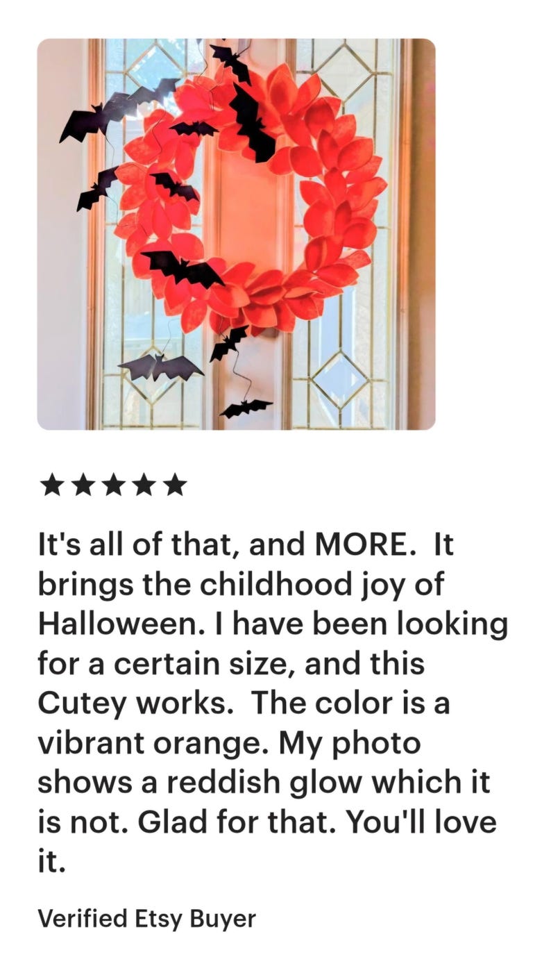 Op de afbeelding: Een rode en zwarte Halloween-krans met vleermuizen die eraan hangen. De krans is gemaakt van papier en heeft een levendige oranje kleur.