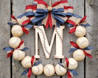 May include: A baseball-themed wreath with a wooden letter "M" in the center. The wreath is decorated with red, white, and blue ribbon and baseballs.